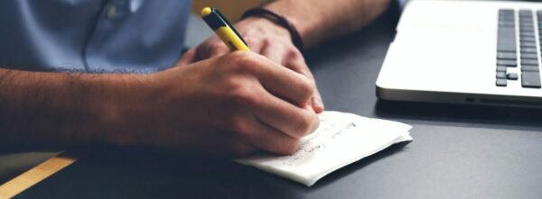 Person Writing on Paper Using Yellow and Black Pen